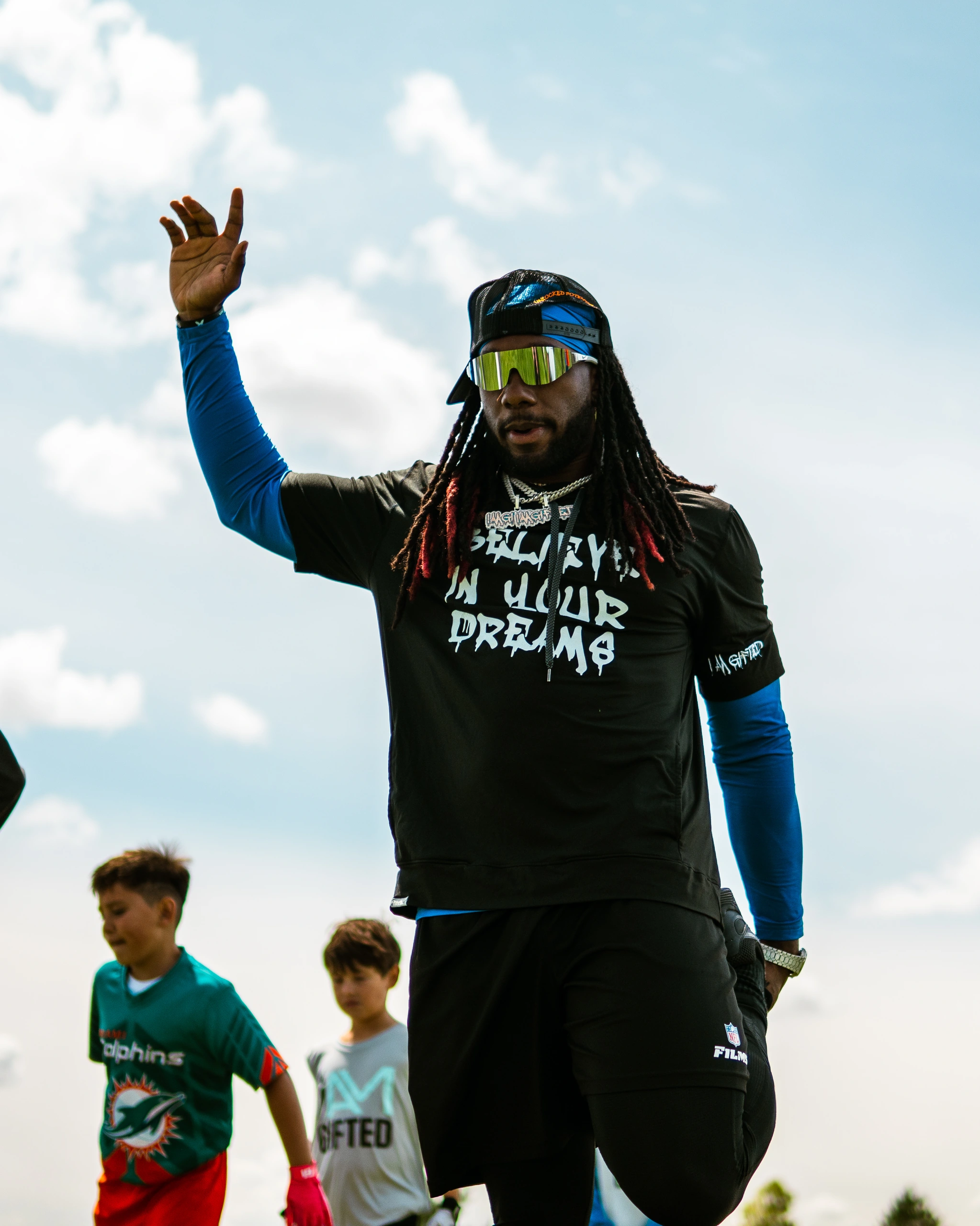 Alexander Mattison walking the field with one hand raised, greeting campers