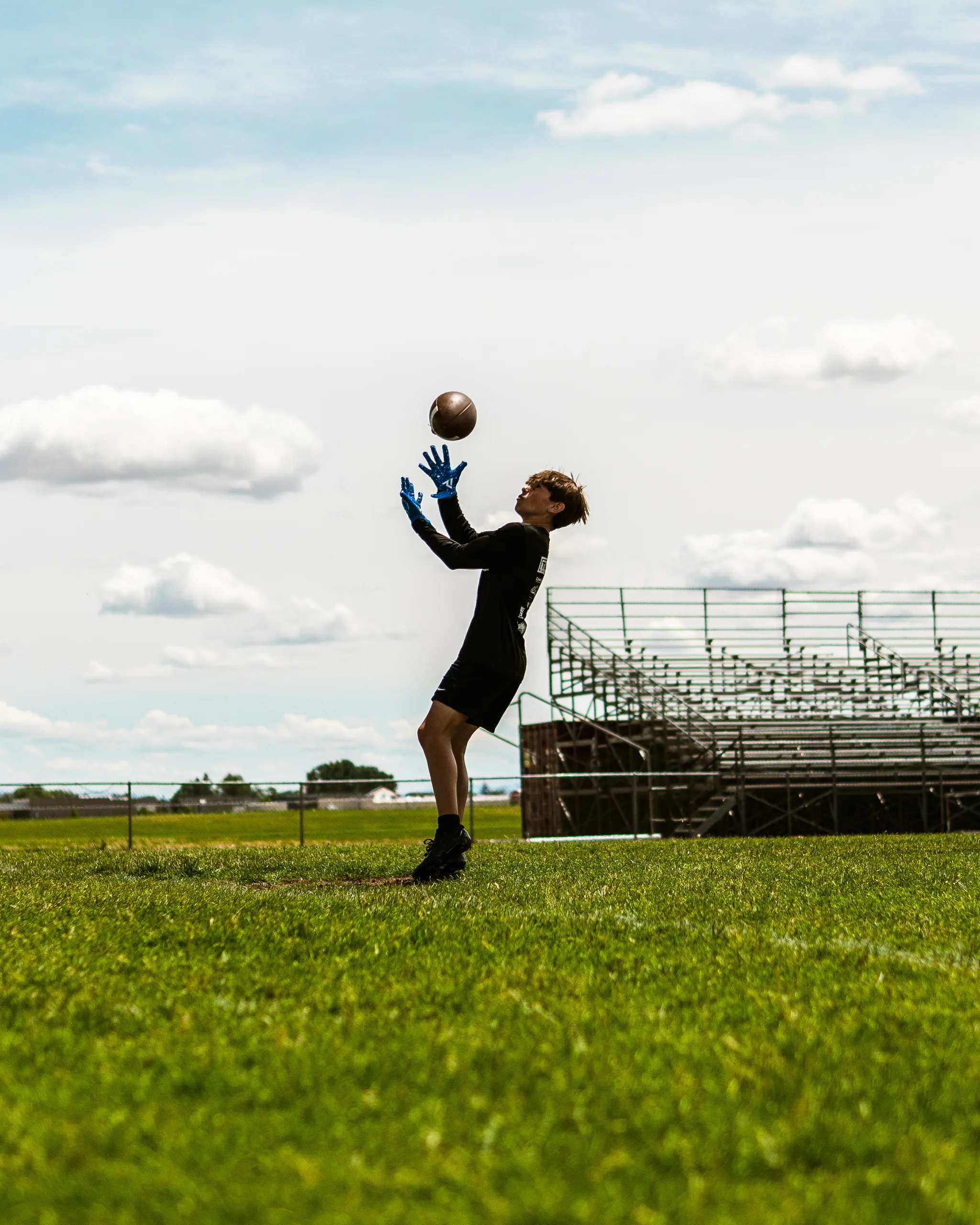 A young camper reaching up to catch a football on an open field under a bright sky