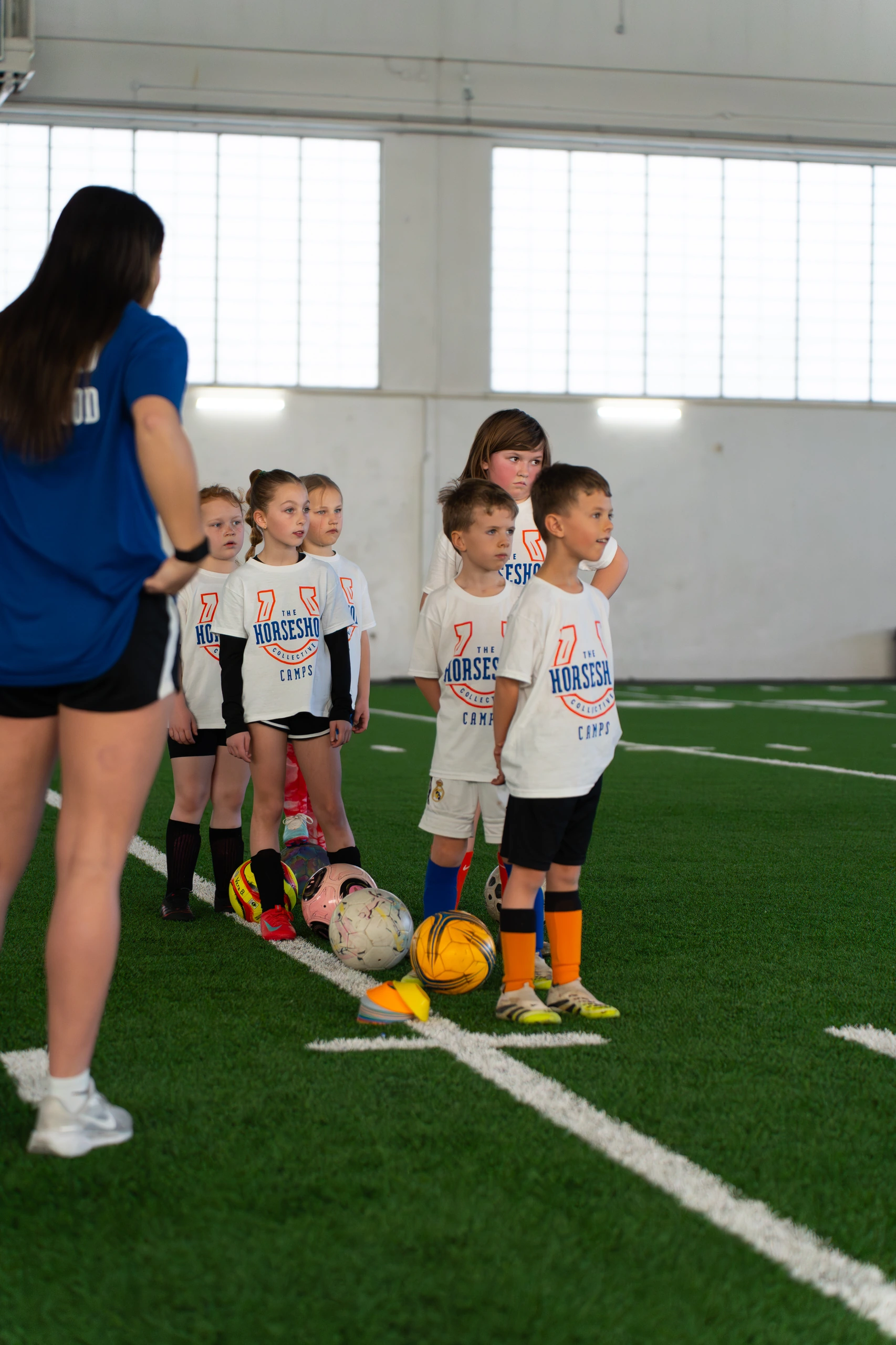 A Boise State player briefing a line of young campers with their soccer balls